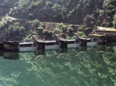 Detalle de los icónicos aliviaderos con forma de salto de esquí de la presa de Salime, reflejados sobre el agua tranquila del río Navia en un entorno de montaña asturiano.